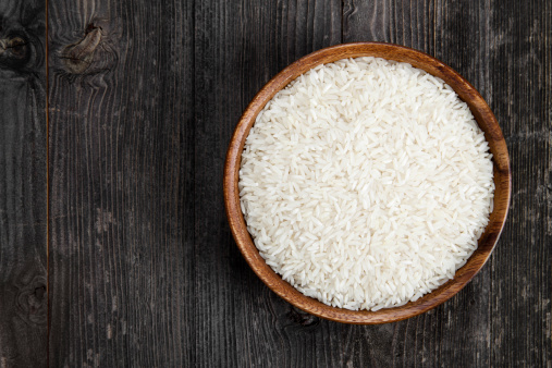 Wooden bowl of rice on a dark wood table.