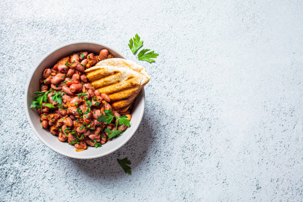 Beans in a sauce with green herbs as garnish. Grilled pita bread in the bowl for a side.